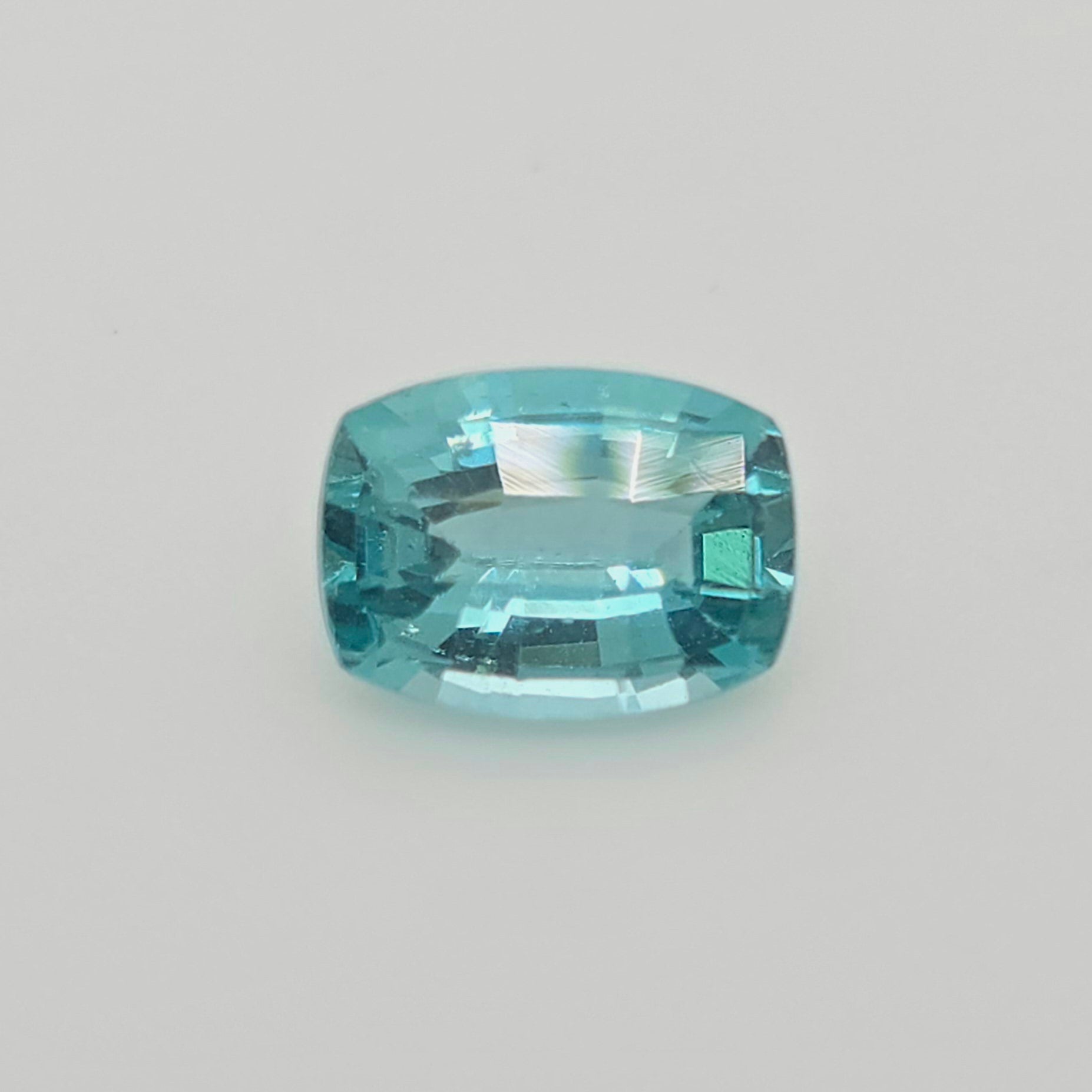 A single cushion-cut light blue gemstone with a faceted, polished finish, centered on a plain light gray background.