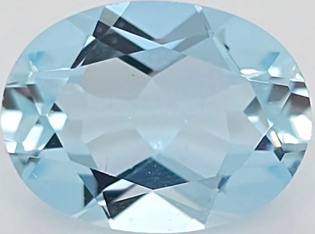 An oval-cut light blue faceted gemstone, showing clear facets and a pale aqua color on a plain light background.