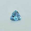 A single triangular light blue gemstone, faceted and cut to sparkle, centered on a clean, light off-white background.