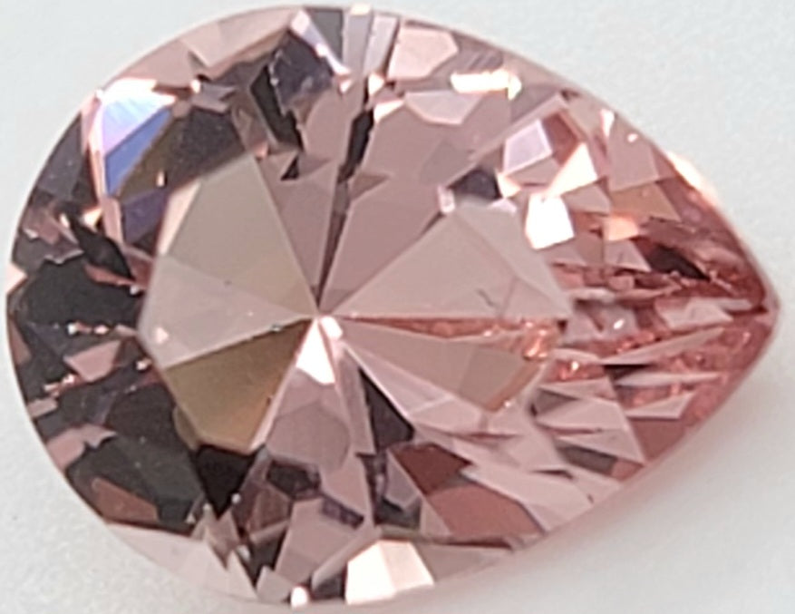 A faceted pear-cut pink gemstone, likely a morganite, shown in close-up on a light gray background.