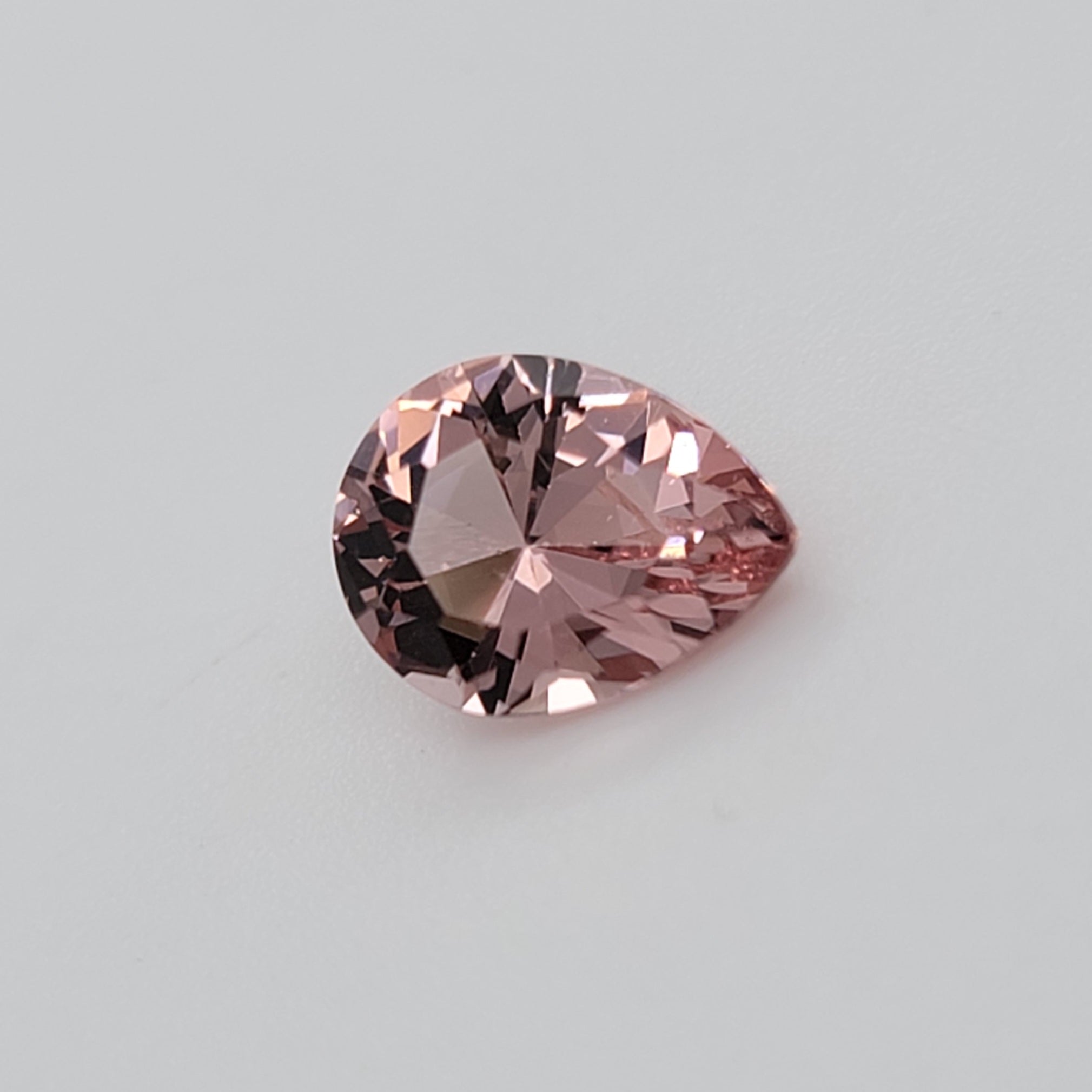 A single pear-cut pink gemstone with faceted reflections, centered on a plain light gray background.