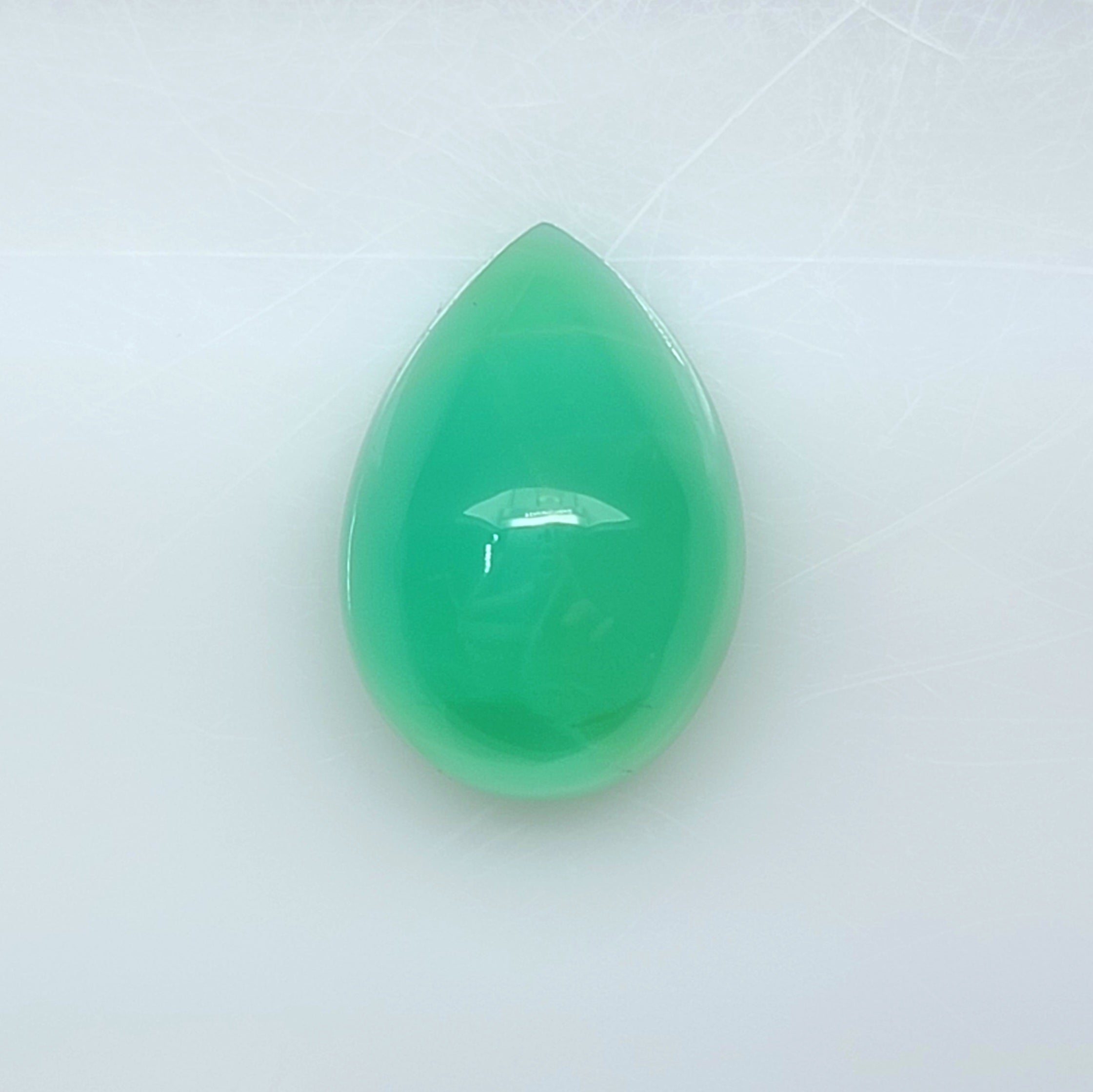A teardrop-shaped green gemstone cabochon with a smooth, polished surface, displayed on a light gray background.