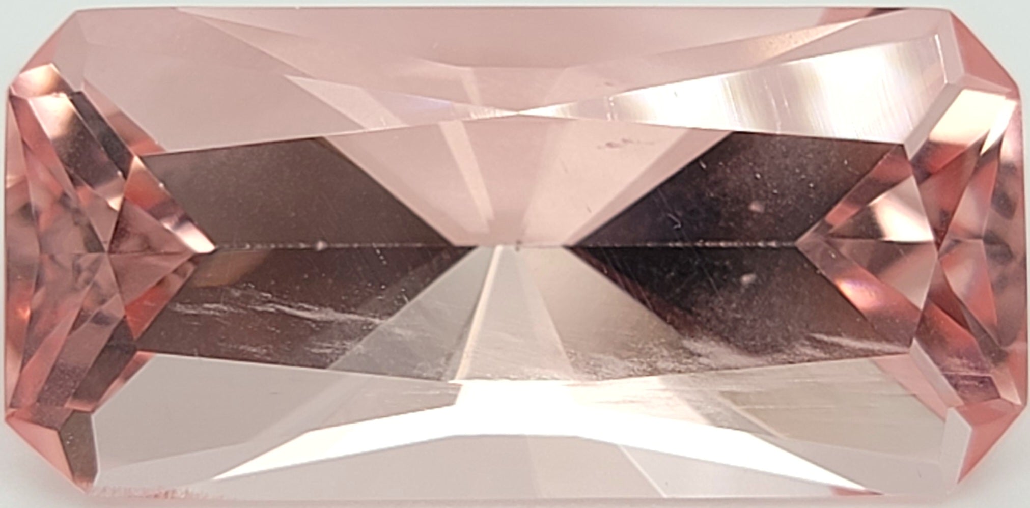A rectangular pink gemstone with a faceted, brilliant cut, shown against a white background.