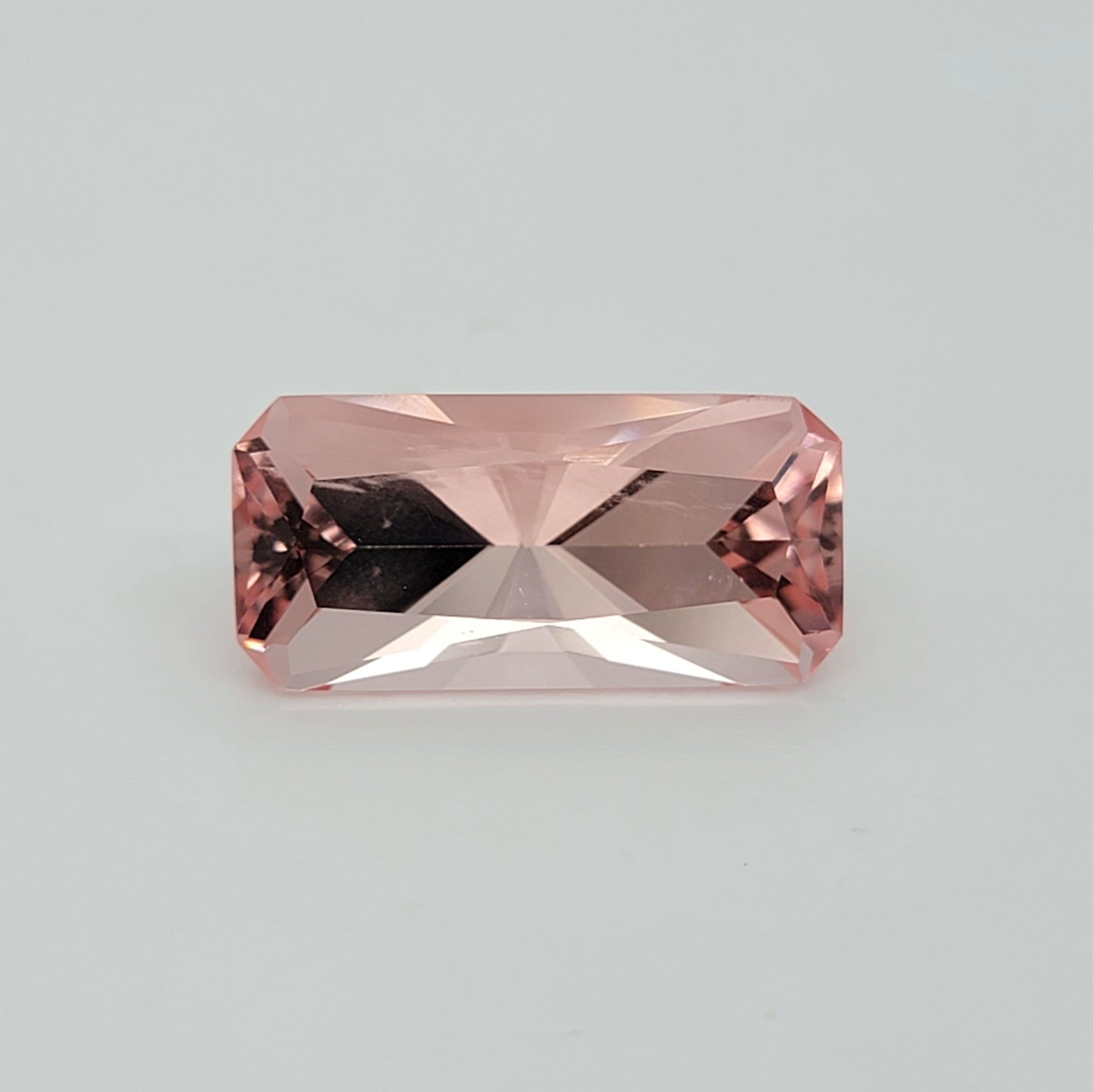A rectangular pink gemstone with a faceted appearance, centered on a light gray background.