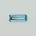 A rectangular emerald-cut light blue gemstone with a faceted, polished finish, centered on a clean, light gray background.