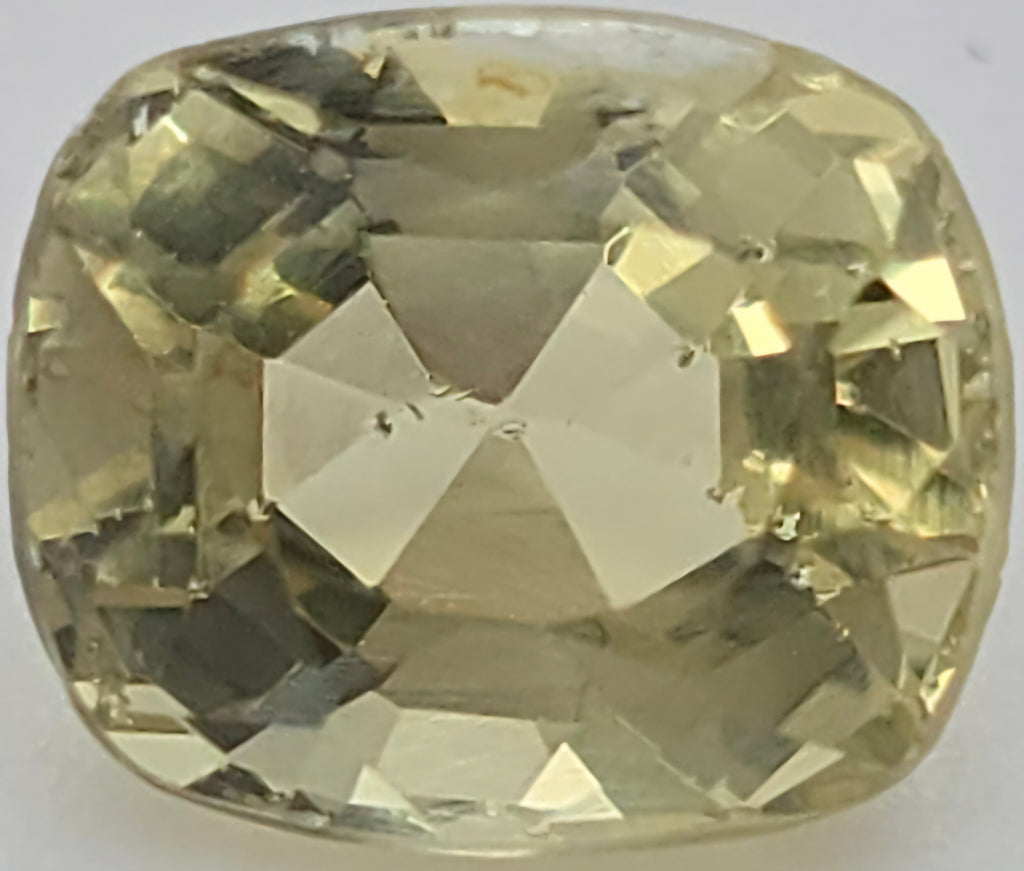 A cushion-cut yellow gemstone with a faceted cushion shape, displayed on a neutral light gray background.
