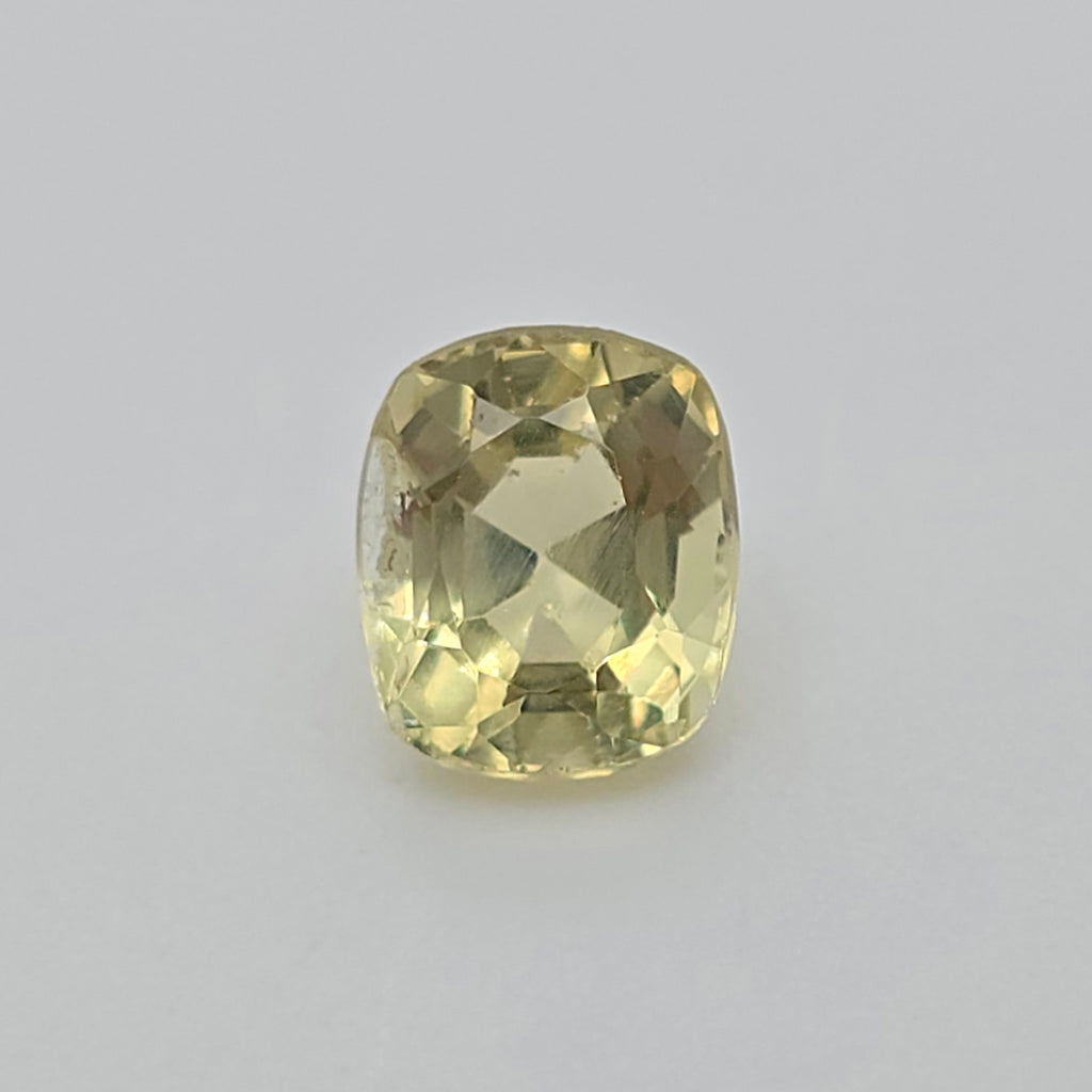 A cushion-cut yellow gemstone with a faceted cushion shape, displayed on a neutral light gray background.