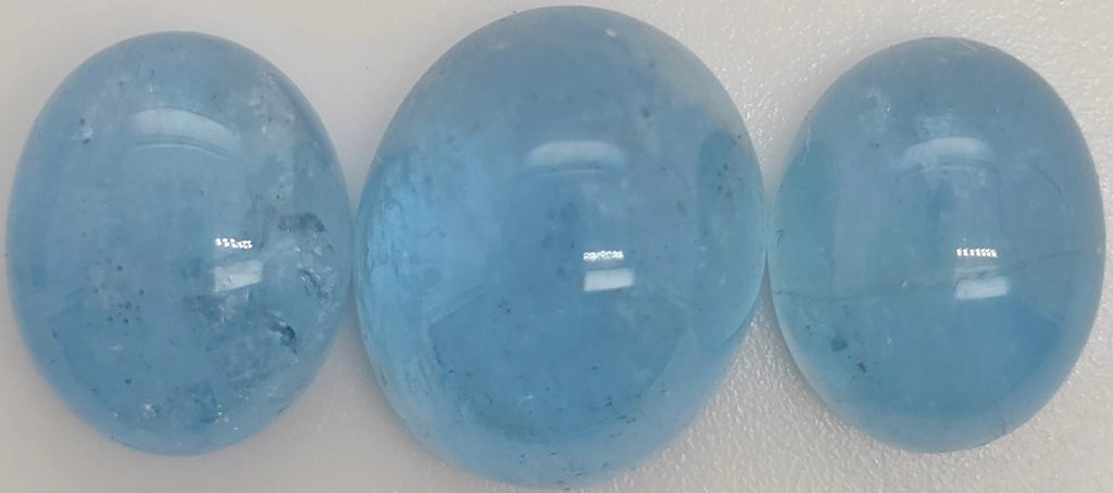 Three smooth, polished oval blue gemstones arranged side by side on a plain light background.