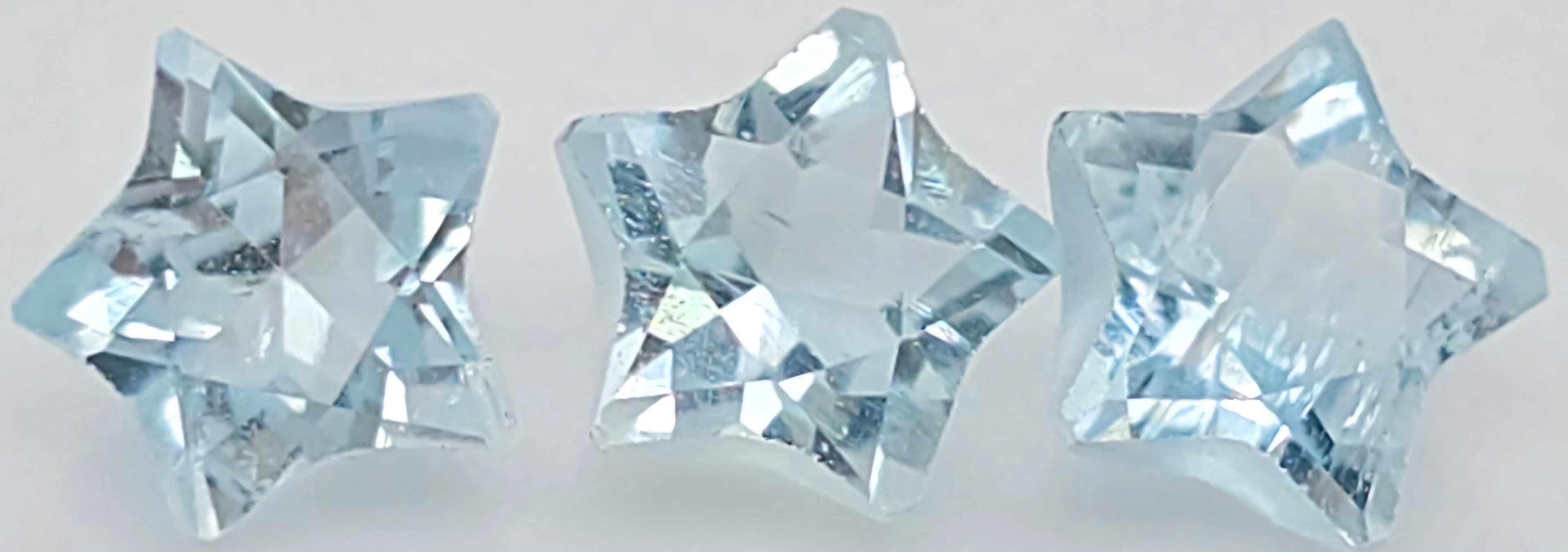 Three faceted star-shaped light blue gemstones arranged side by side on a plain white background.