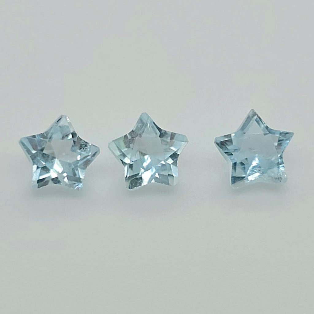 Three faceted star-shaped light blue gemstones arranged horizontally on a plain light gray background.