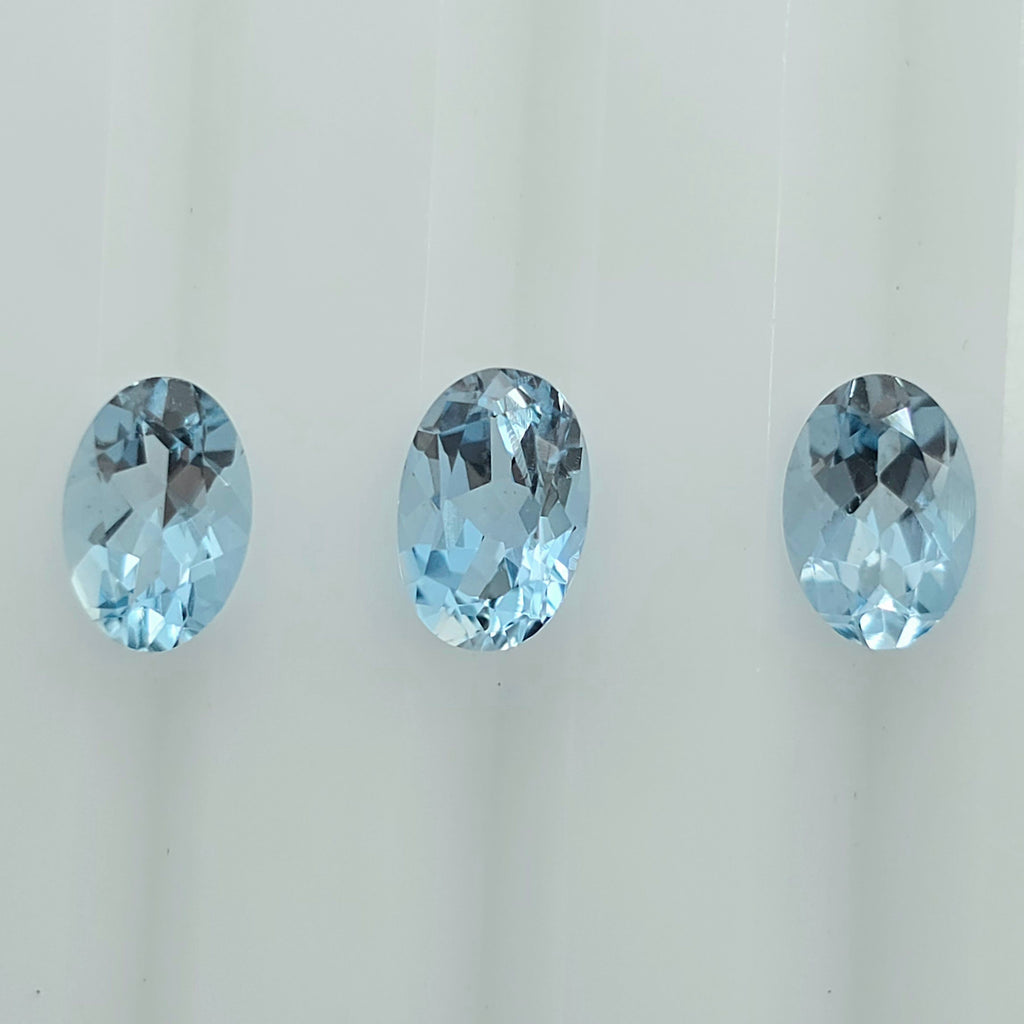 Three oval-cut light blue gemstones arranged horizontally against a plain white background.