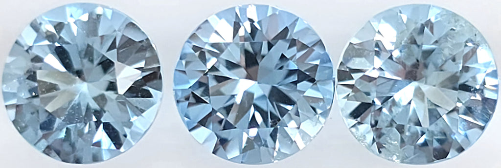 Three round brilliant-cut light blue gemstones displayed side by side against a plain white background.