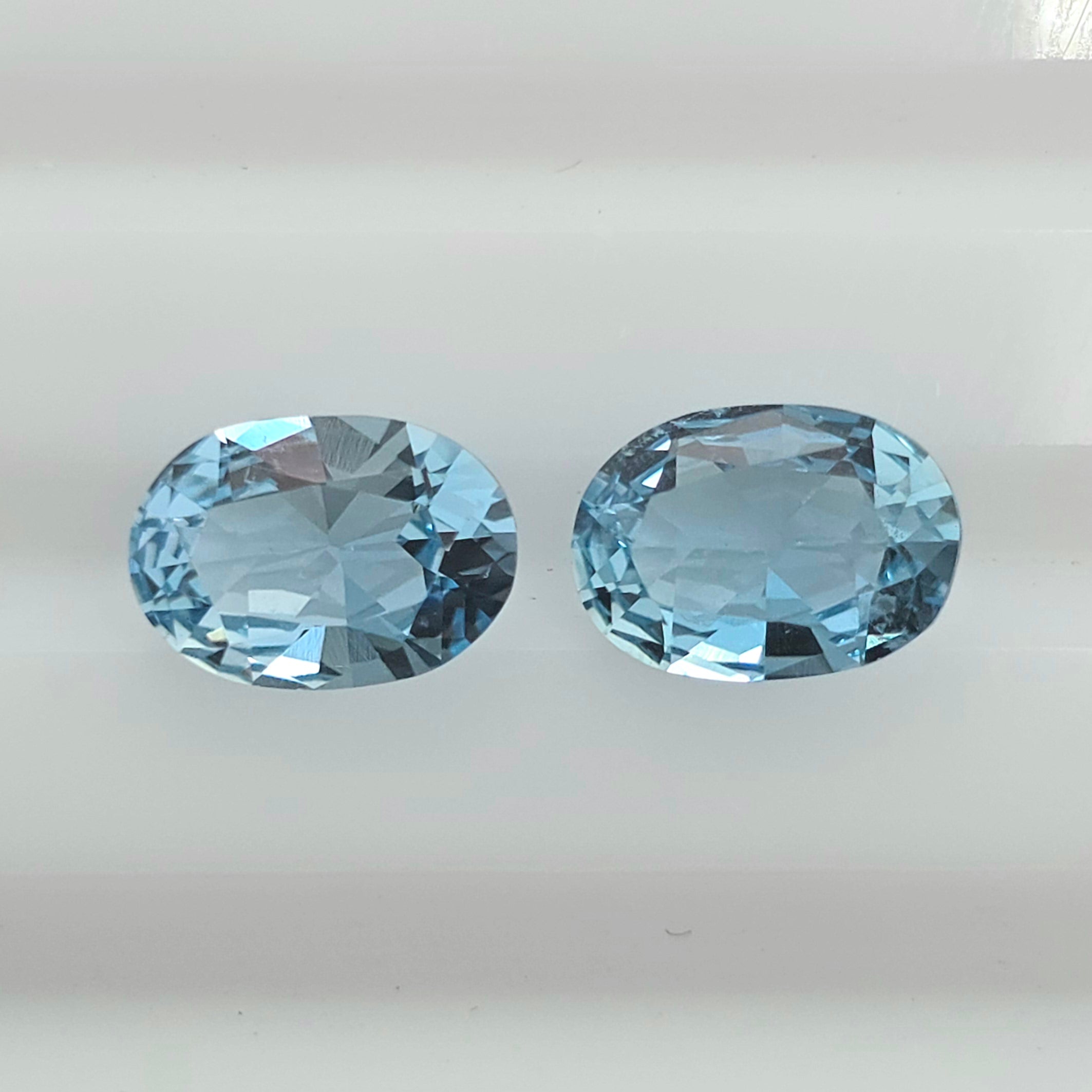 Two oval-cut light blue gemstones displayed side by side on a plain white background.