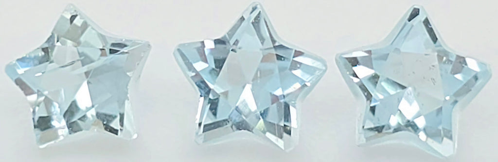 Three faceted star-shaped clear gemstones with a light icy blue tint, arranged horizontally on a plain white background.