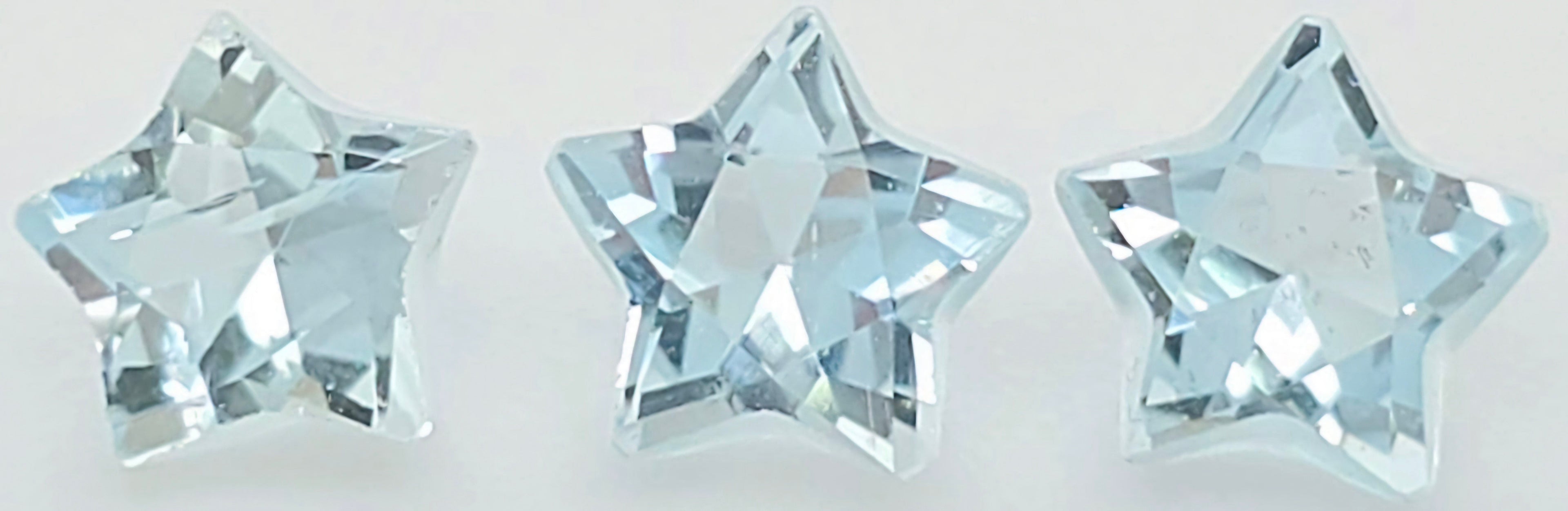 Three faceted star-shaped clear gemstones with a light icy blue tint, arranged horizontally on a plain white background.