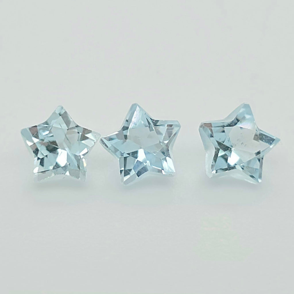 Three faceted light blue star-shaped gemstones arranged horizontally on a plain light gray background.