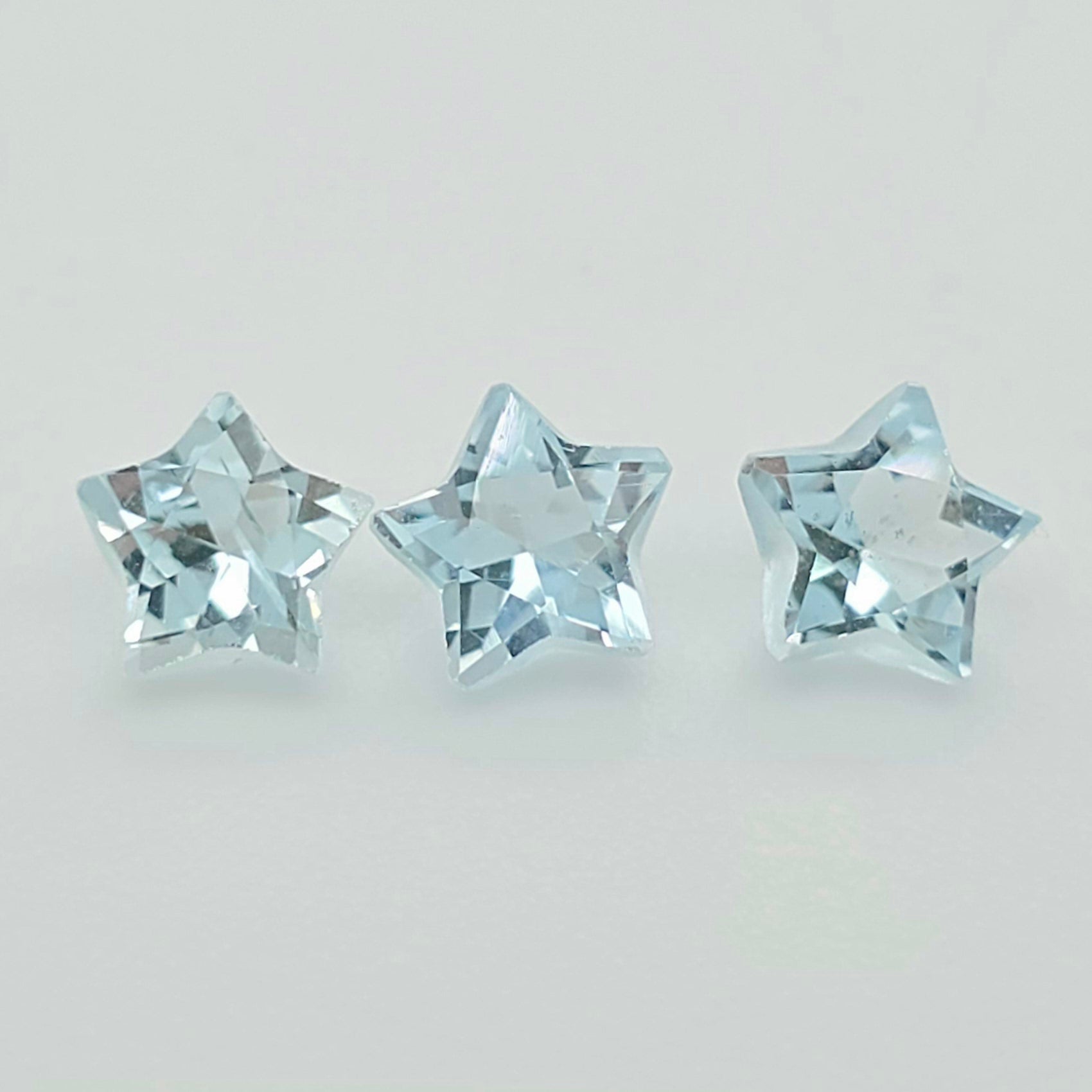 Three faceted light blue star-shaped gemstones arranged horizontally on a plain light gray background.