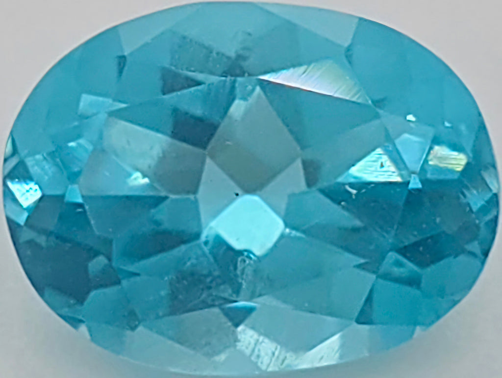 A faceted oval-cut light blue gemstone centered on a light gray background