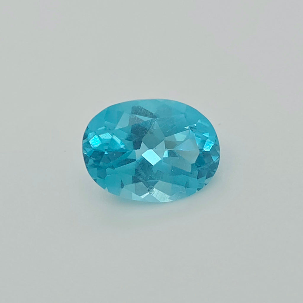 A faceted oval-cut light blue gemstone centered on a light gray background