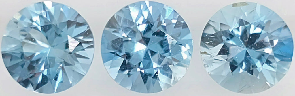 Three round brilliant-cut light blue gemstones shown side by side against a plain light background.