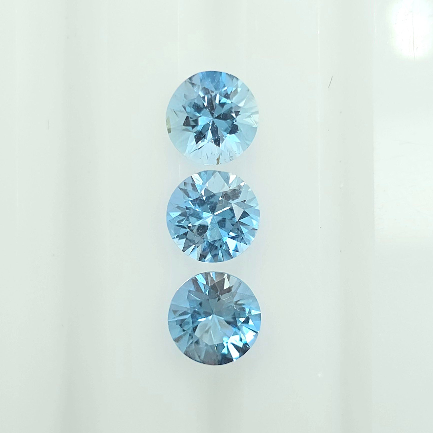 Three round-cut light blue gemstones arranged vertically on a plain white background.