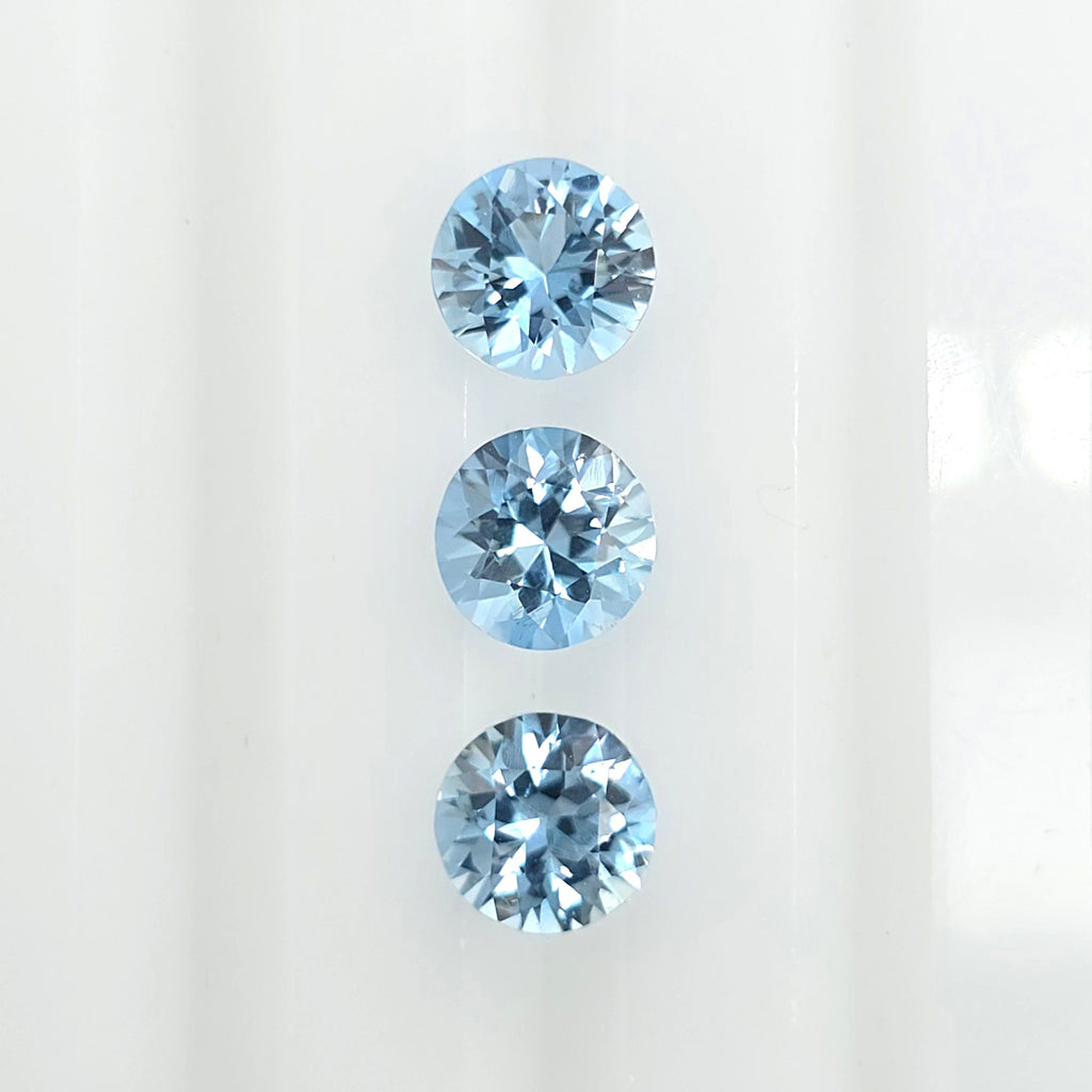 Three round light blue faceted gemstones arranged vertically on a clean white background.