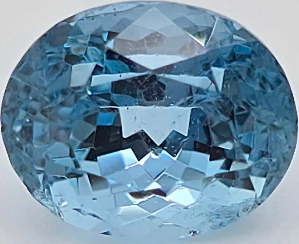 A faceted oval-cut light blue gemstone, shown in a close-up studio shot against a plain light gray background.