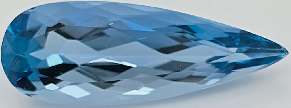 A faceted teardrop-shaped blue gemstoneshown on a plain light gray background.