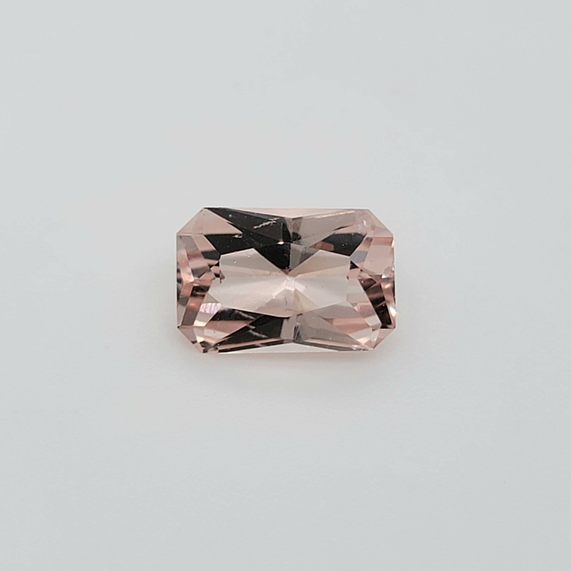 A single rectangular radiant cut pink gemstone with faceted edges, centered on a plain light gray background.