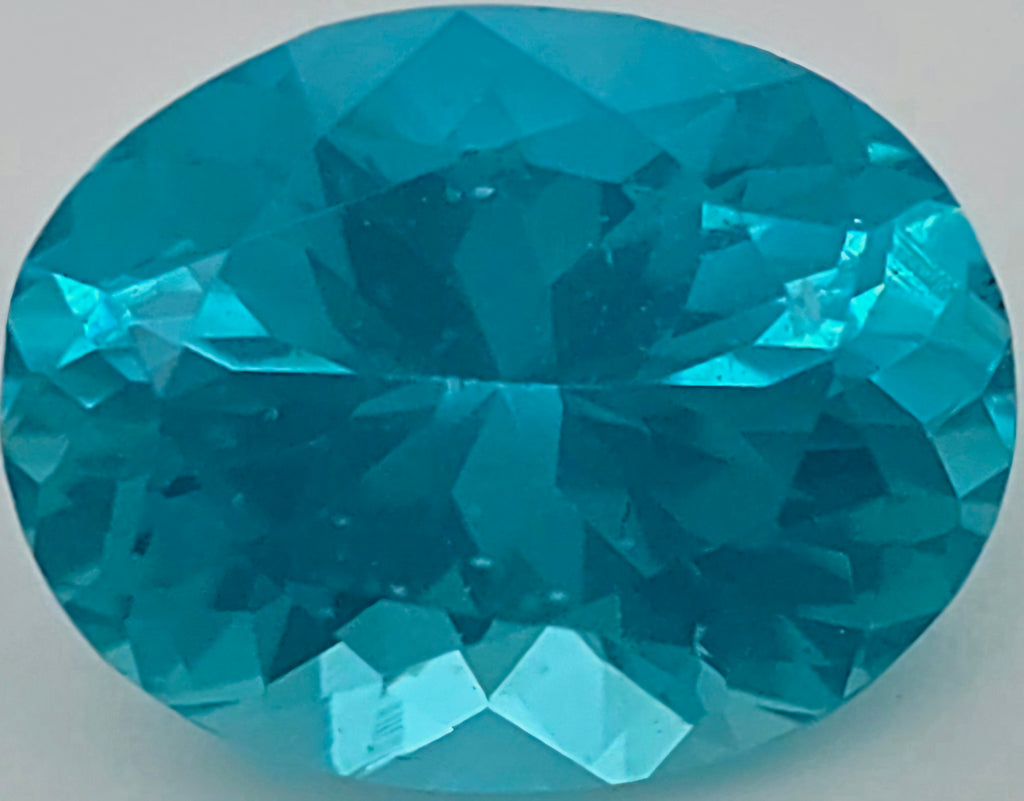 An oval-cut, faceted turquoise gemstone on a plain light gray background.