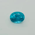 An oval-cut, faceted turquoise gemstone on a plain light gray background.