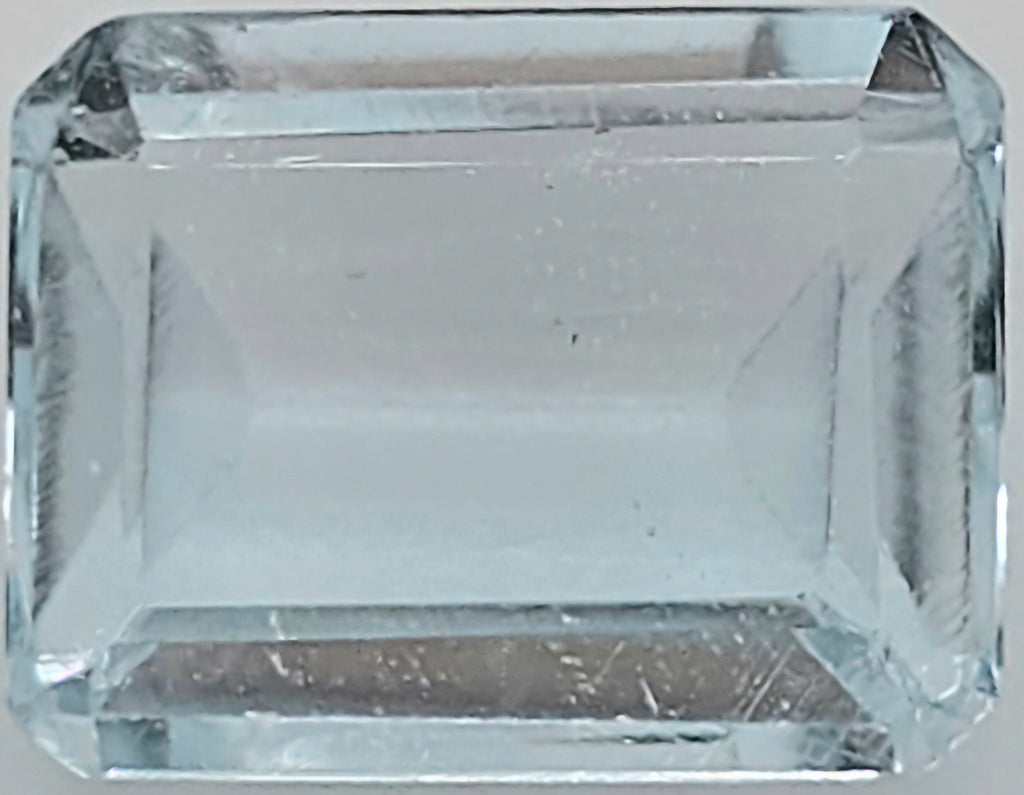A clear rectangular emerald-cut gemstone with faceted edges, shown against a neutral light gray background.