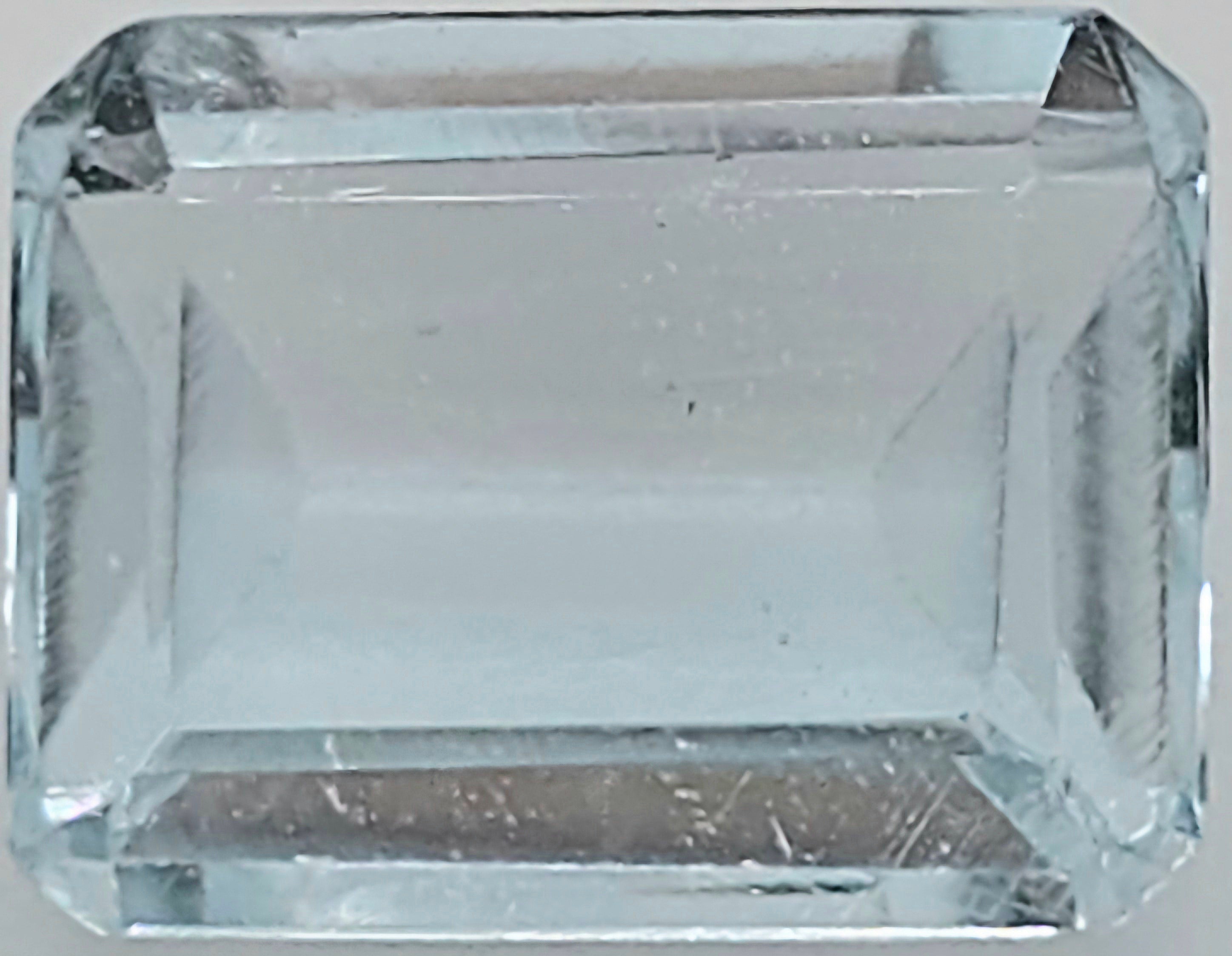 A clear rectangular emerald-cut gemstone with faceted edges, shown against a neutral light gray background.