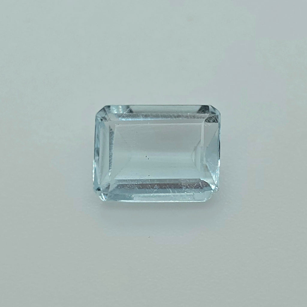A rectangular emerald-cut gemstone with a light blue tint, photographed on a plain light gray background.