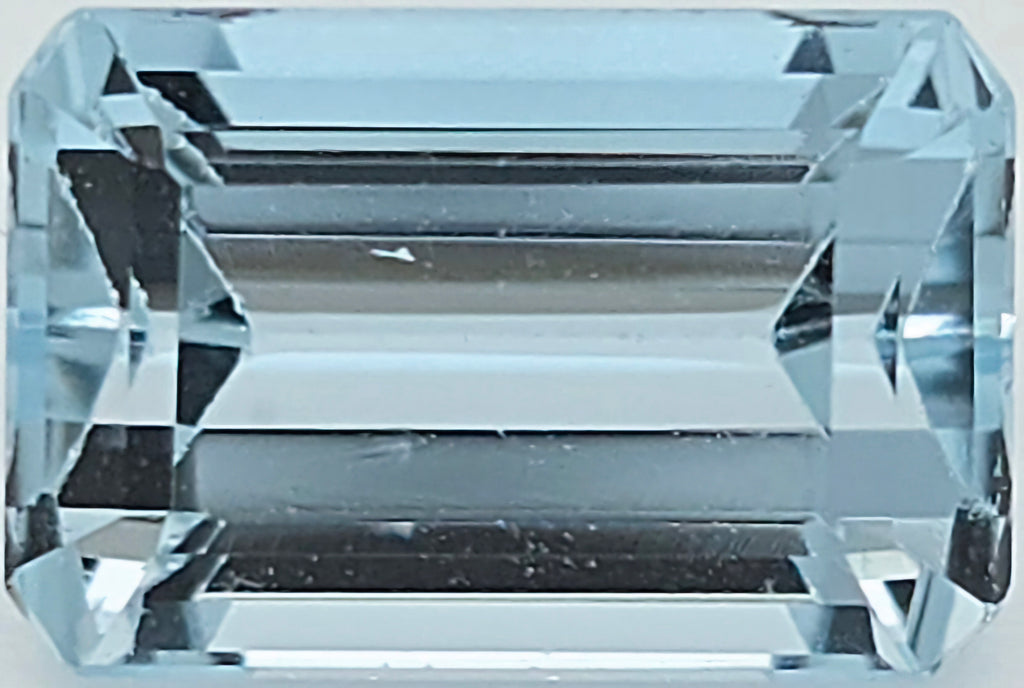 A light blue emerald-cut faceted gemstone, showing clear geometric facets and a light blue hue.