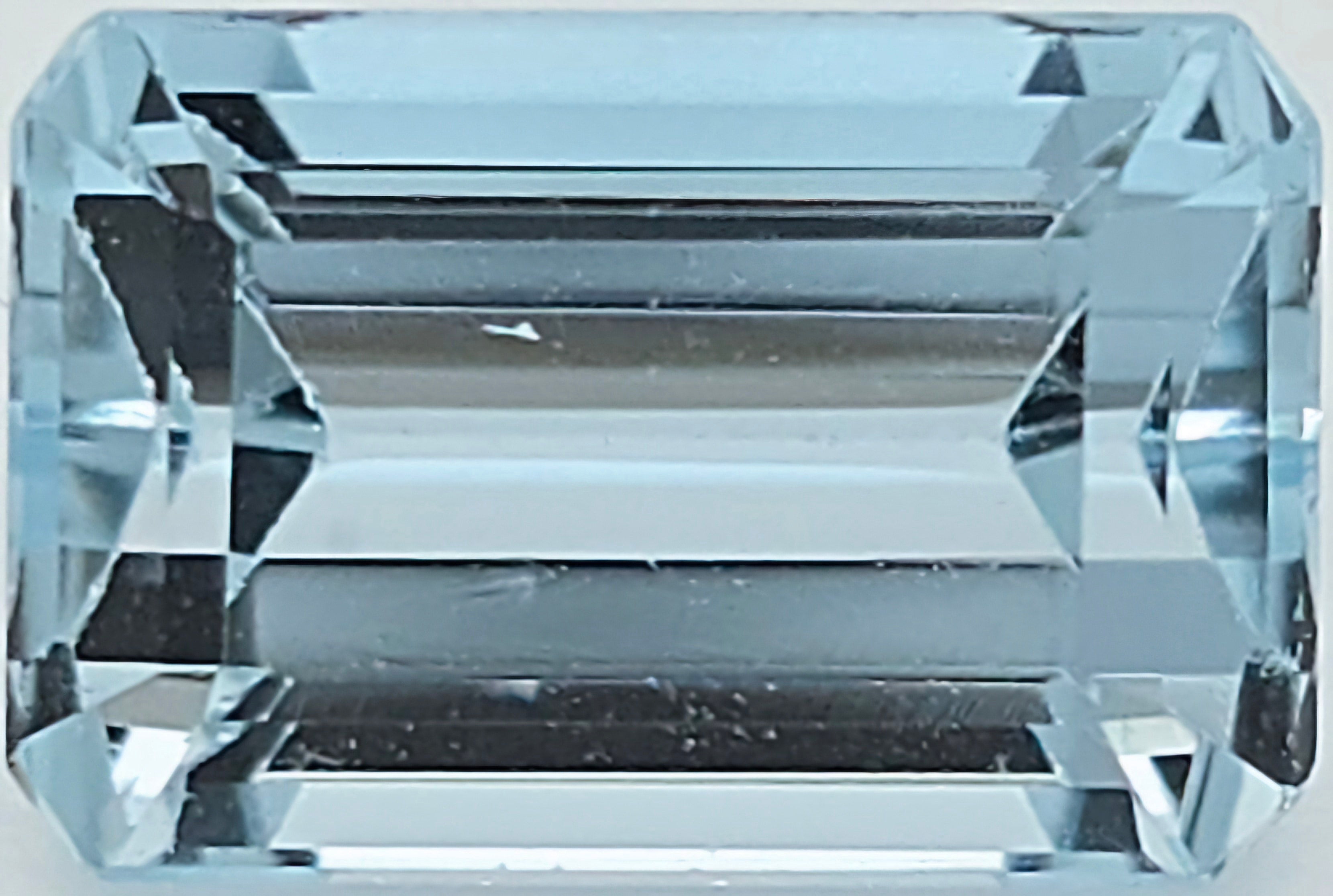 A light blue emerald-cut faceted gemstone, showing clear geometric facets and a light blue hue.