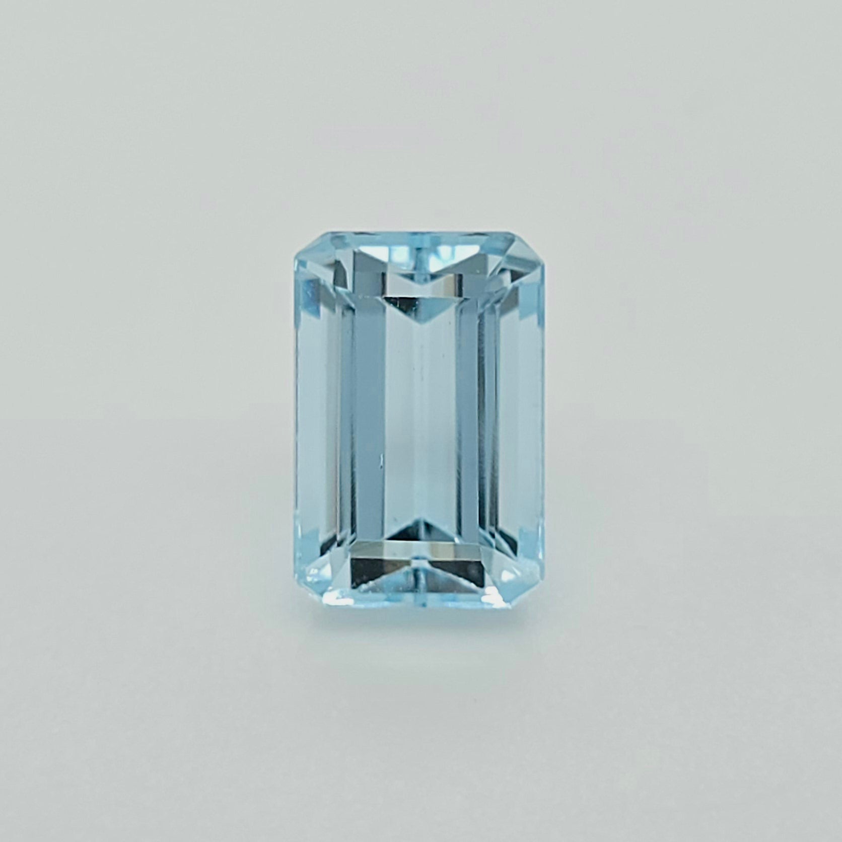 A single light blue emerald-cut gemstone centered on a plain light gray background.