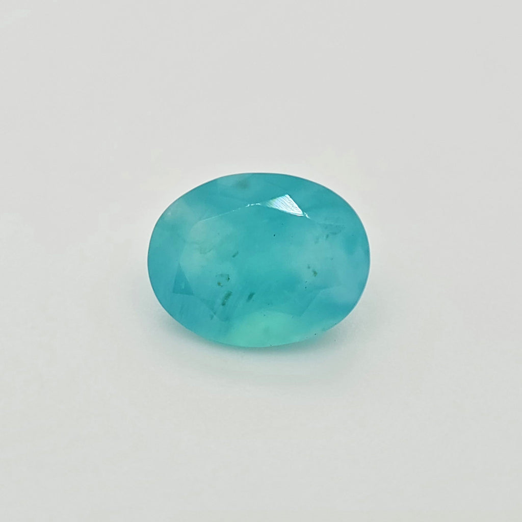 A faceted oval greenish blue gemstone with natural inclusions, shown on a plain white background.