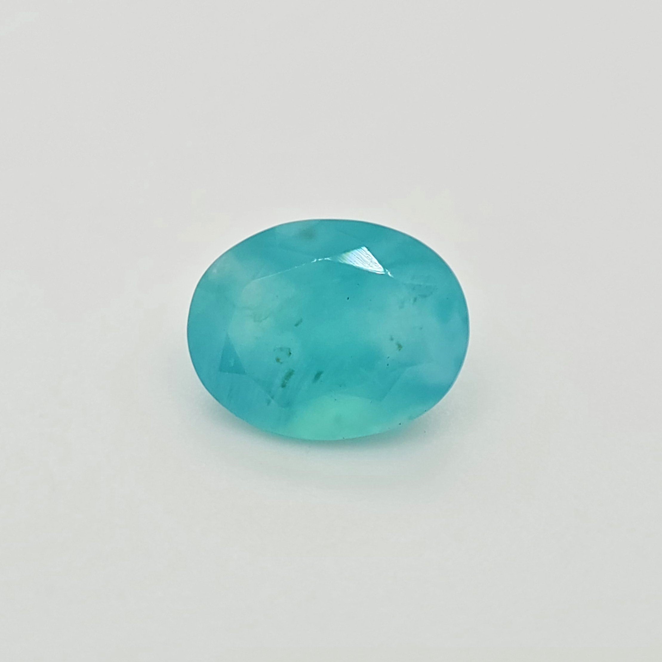 A faceted oval greenish blue gemstone with natural inclusions, shown on a plain white background.