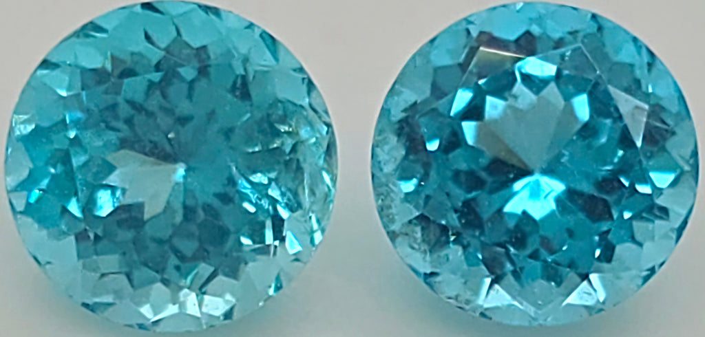Two round brilliant-cut light blue gemstones shown side by side against a plain light background.