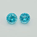Two round brilliant-cut light blue gemstones displayed side-by-side on a clean, light gray background.