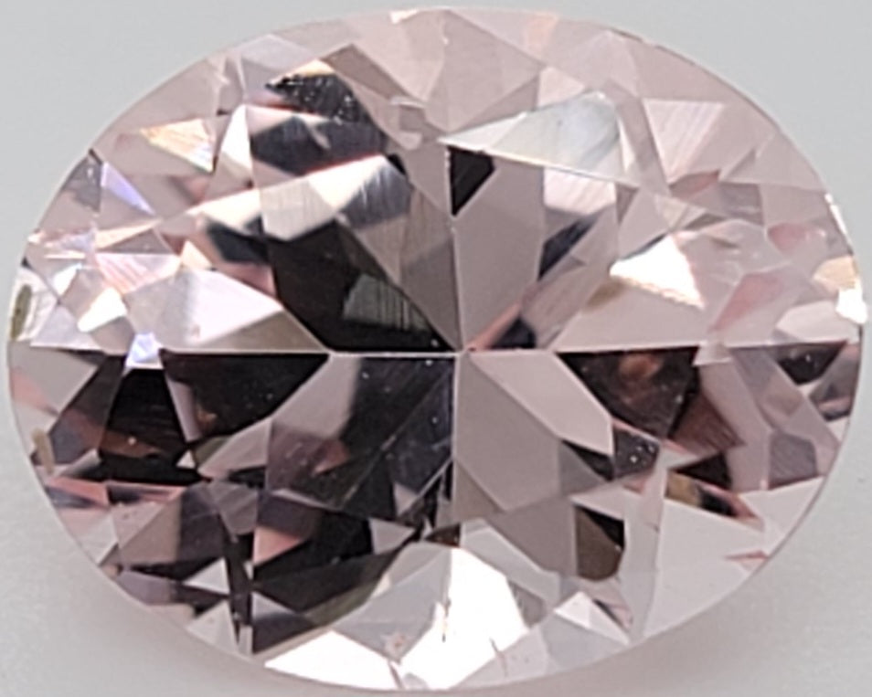 An oval-cut pink gemstone with a faceted, reflective surface, shown against a plain light gray background.