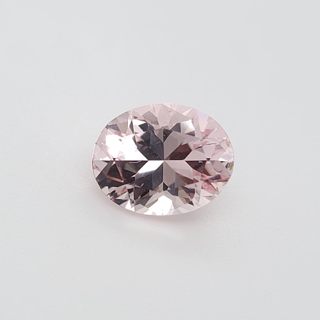 An oval-cut pink gemstone with faceted reflections, centered on a plain light gray background.