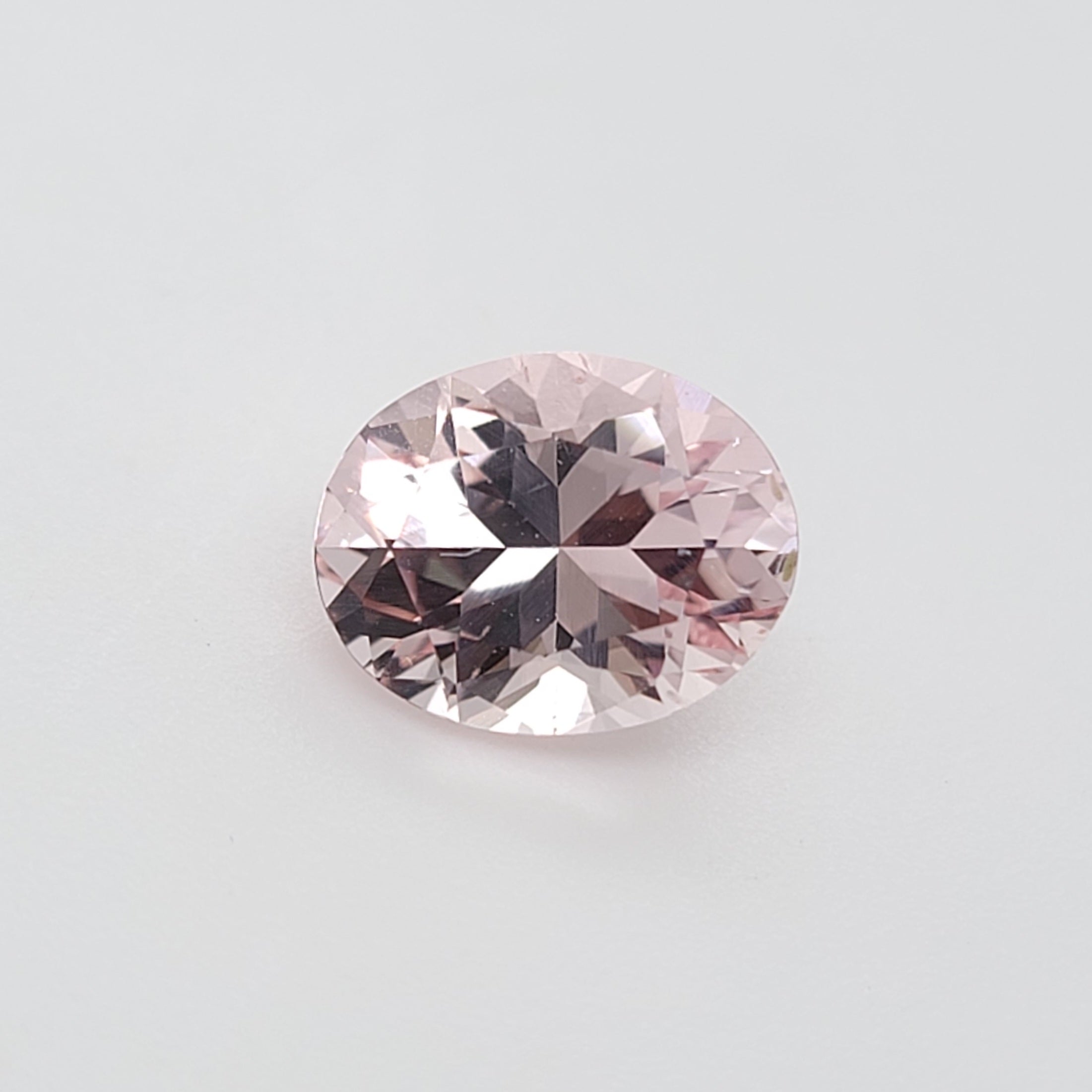 An oval-cut pink gemstone with faceted reflections, centered on a plain light gray background.