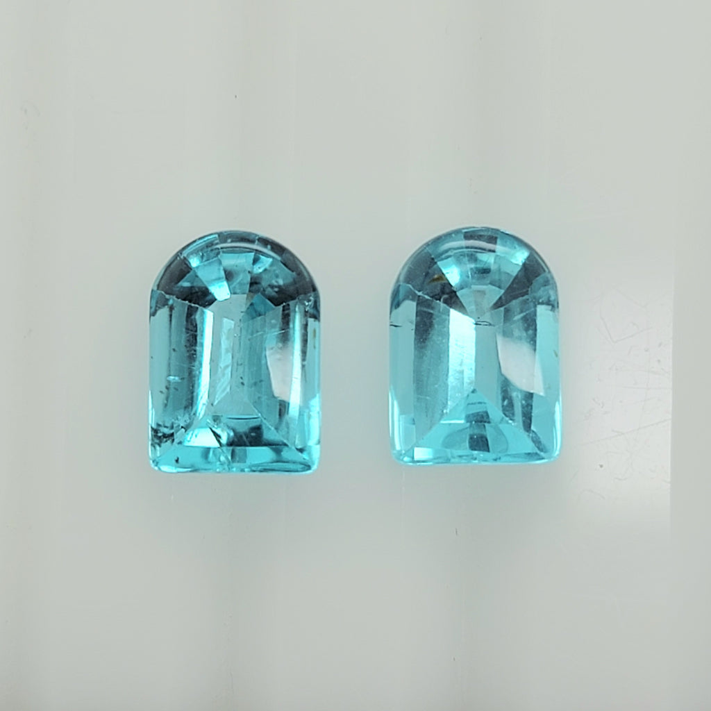 A pair of light blue faceted gemstone cabochons with a rounded top and rectangular body, displayed side-by-side on a plain light background.