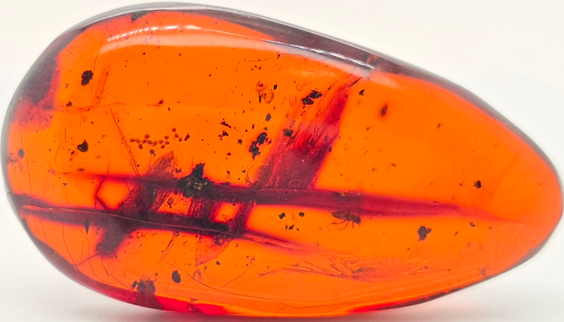 A polished teardrop-shaped orange gemstone with dark inclusions and speckles, shown on a plain white background.