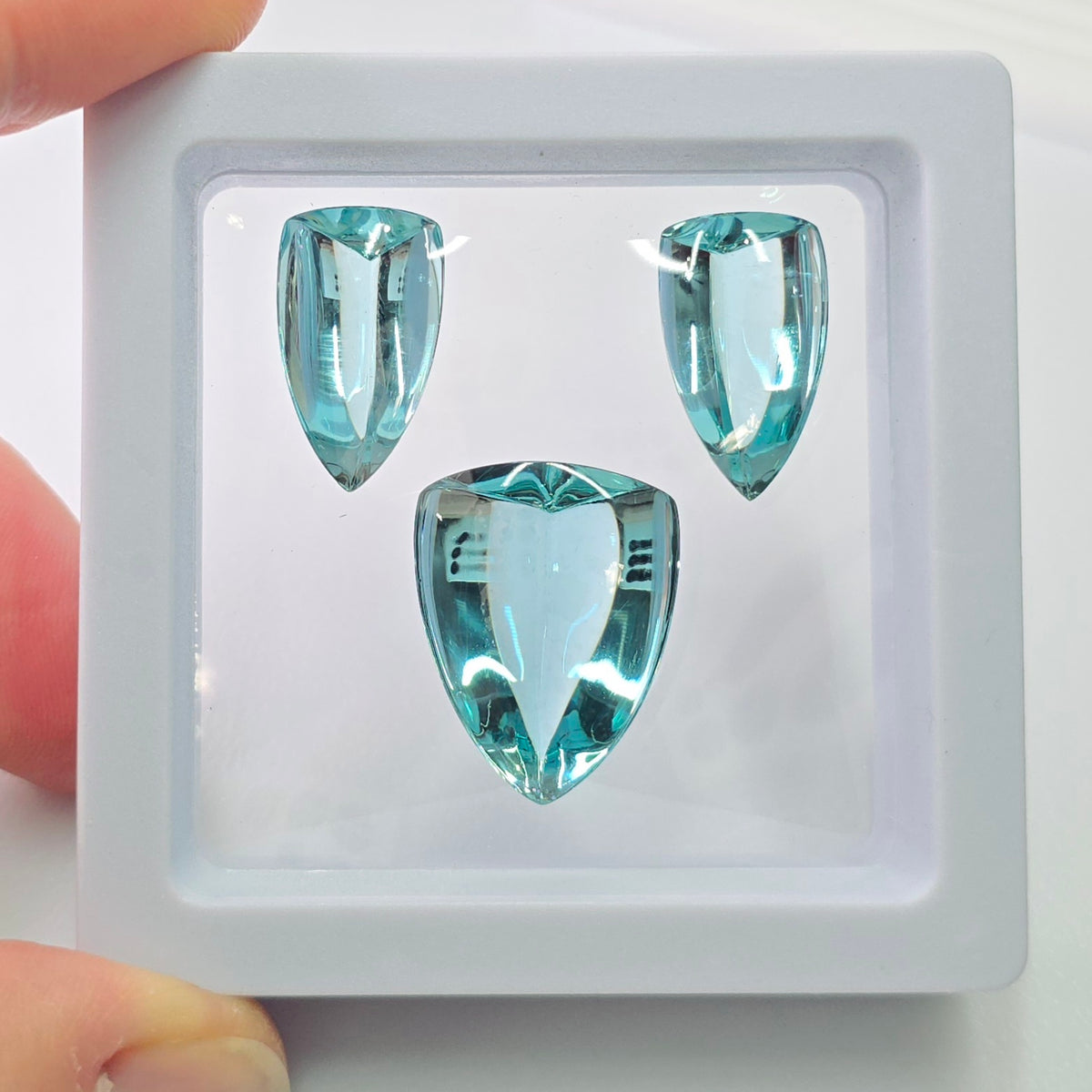 Three shield shaped green-blue cabochon gemstones in a white frame on a white background