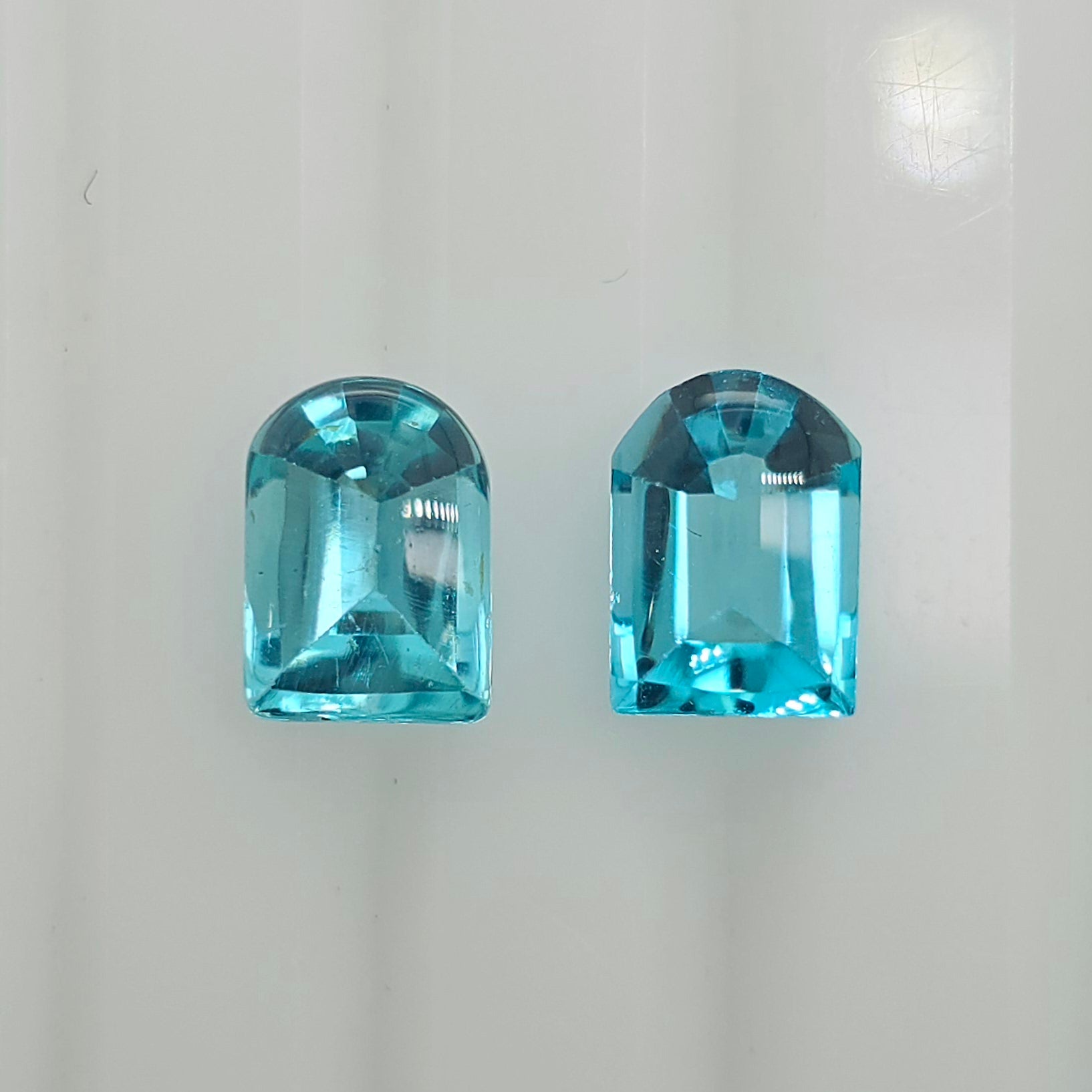Two rounded rectangular cut greenish blue gemstones displayed side by side on a plain white surface.