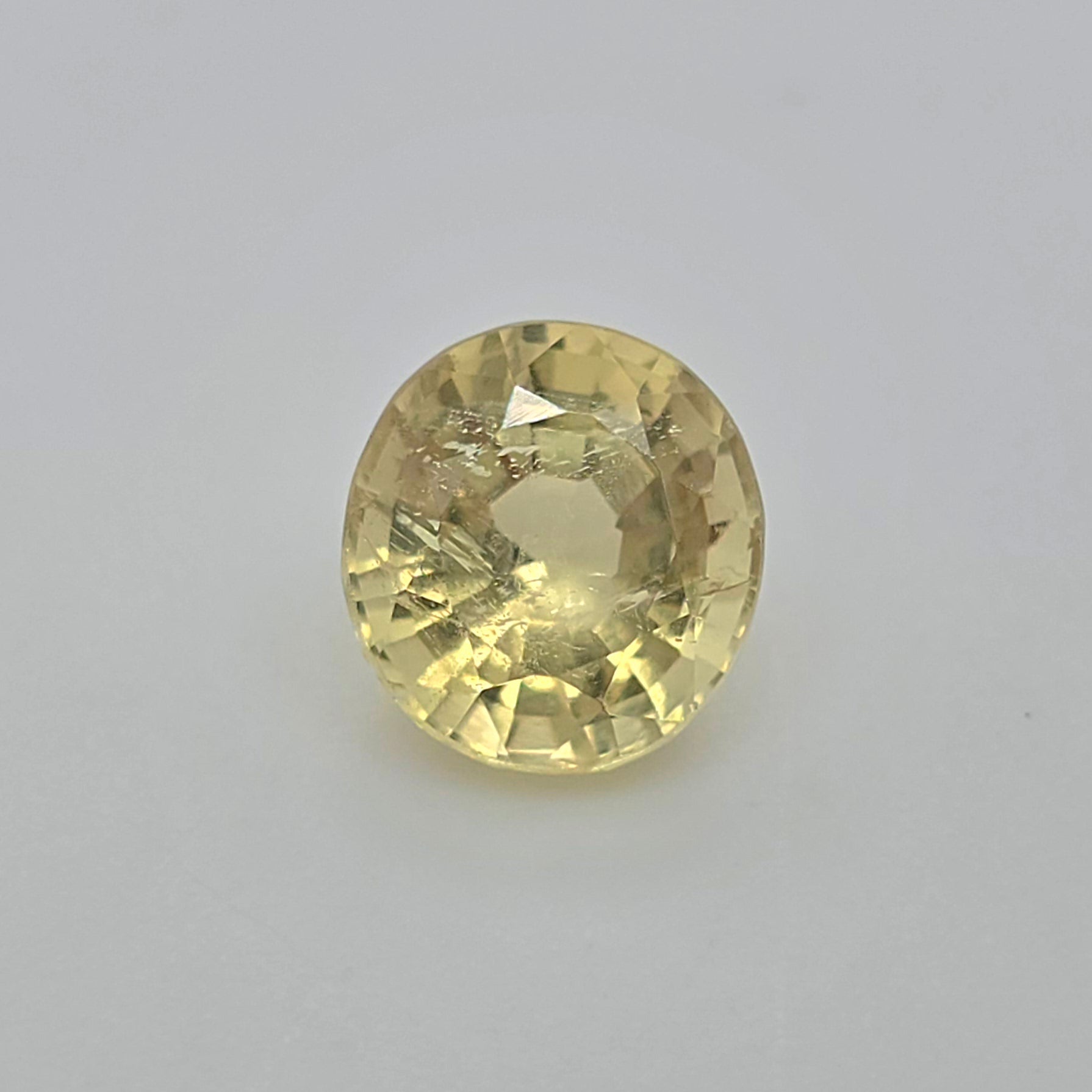 An oval faceted yellow gemstone, likely a shown in a top-down view against a plain white background.