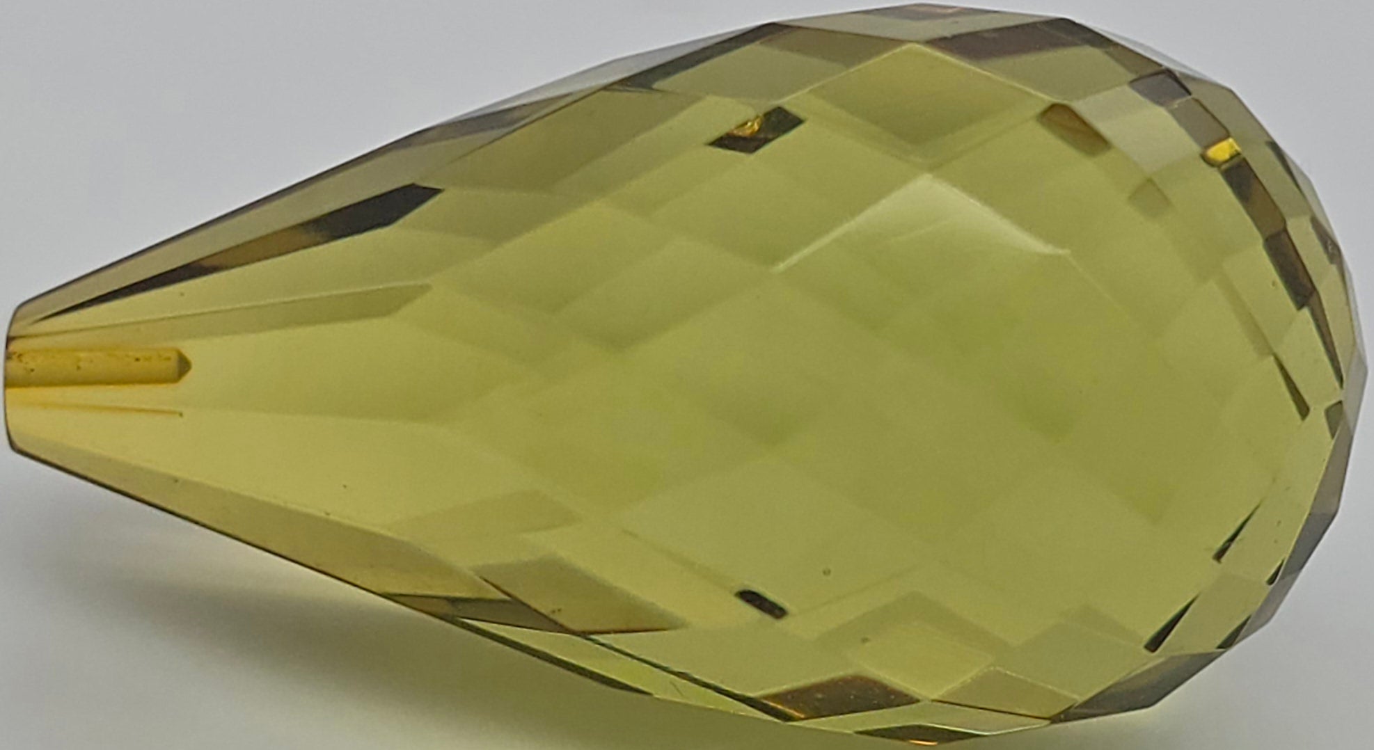 A faceted teardrop-shaped bead in a translucent yellow-green color, shown on a plain light gray background.